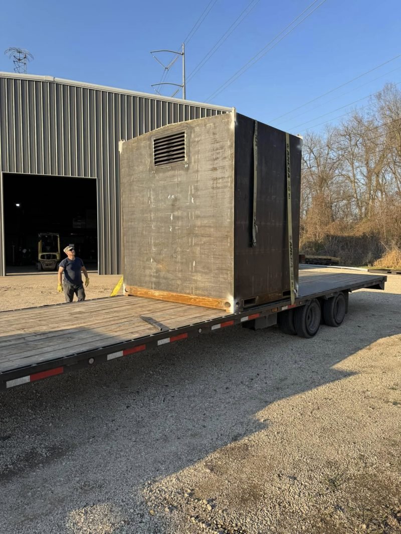 Steel equipment enclosure strapped on a flatbed trailer